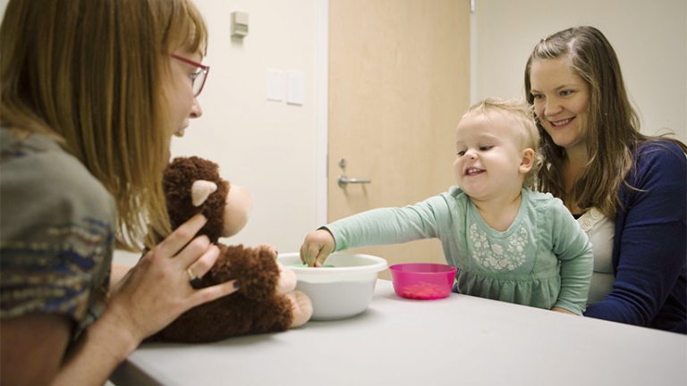 Toddler Gloria Slevinsky sits on her mother Janine Slevinsky's lap across from Kiley Hamlin (left), Canada Research Chair of Developmental Psychology, at UBC in Vancouver. Hamlin's research studies babies and toddlers and sharing. In this experiment Slevinsky was provided with treats that she ccould choose to share with a stuffed toy. (Photograph by Della Rollins)