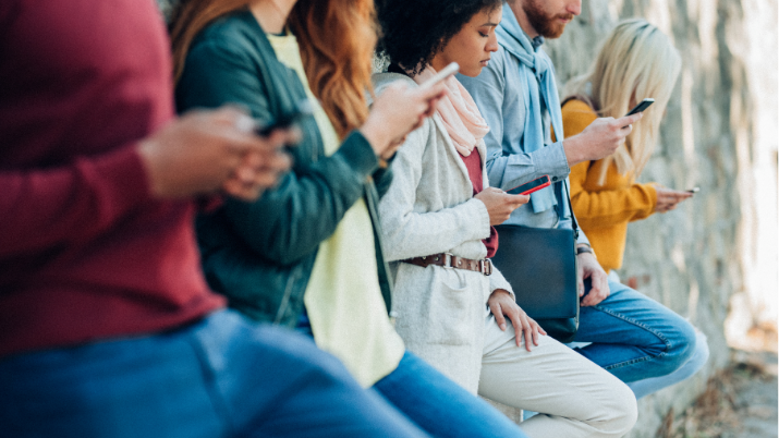 Photo of a group of people, sitting together in a casual setting, are all focused on their smartphones, scrolling through social media